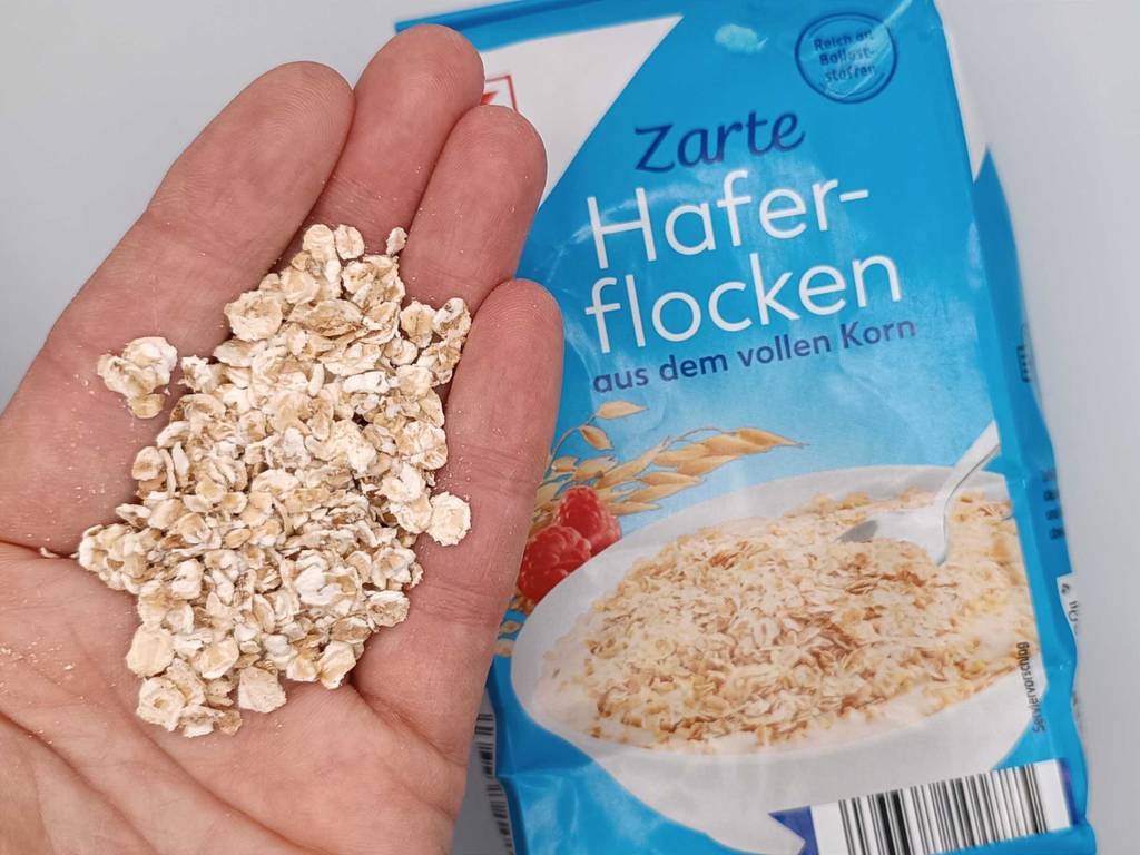 In einer Hand befinden sich getestete Haferflocken neben der Verpackung.