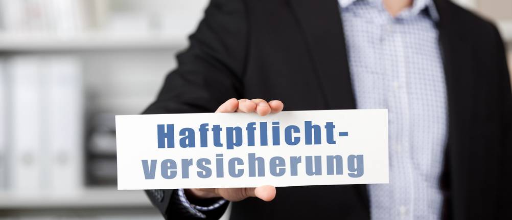 Haftpflichtversicherung-Test: Ein Mann mit Jacket hält ein Schild mit der Aufschrift Haftplichtversicherung in der Hand.
