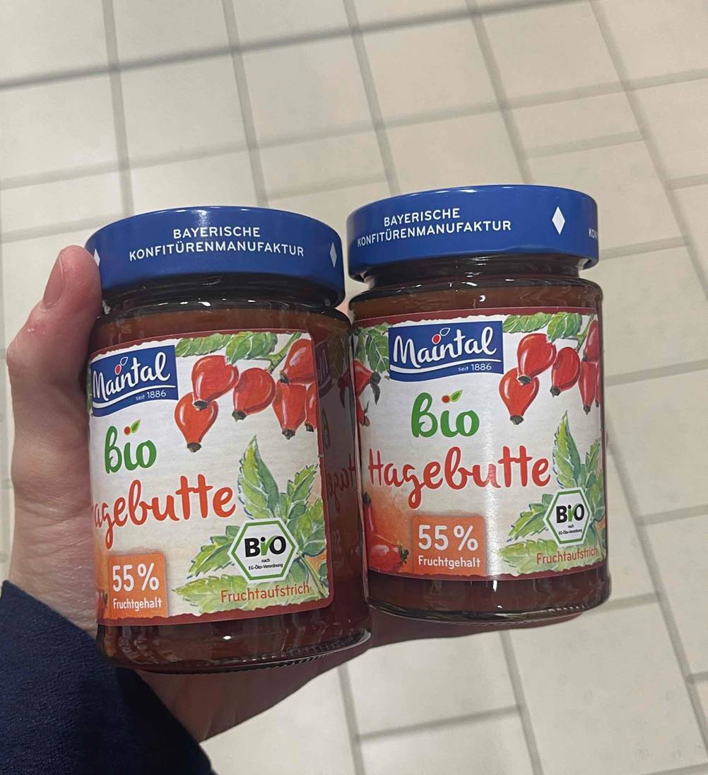 Eine Hand hält zwei Gläser Hagebuttenmarmelade zum testen.
