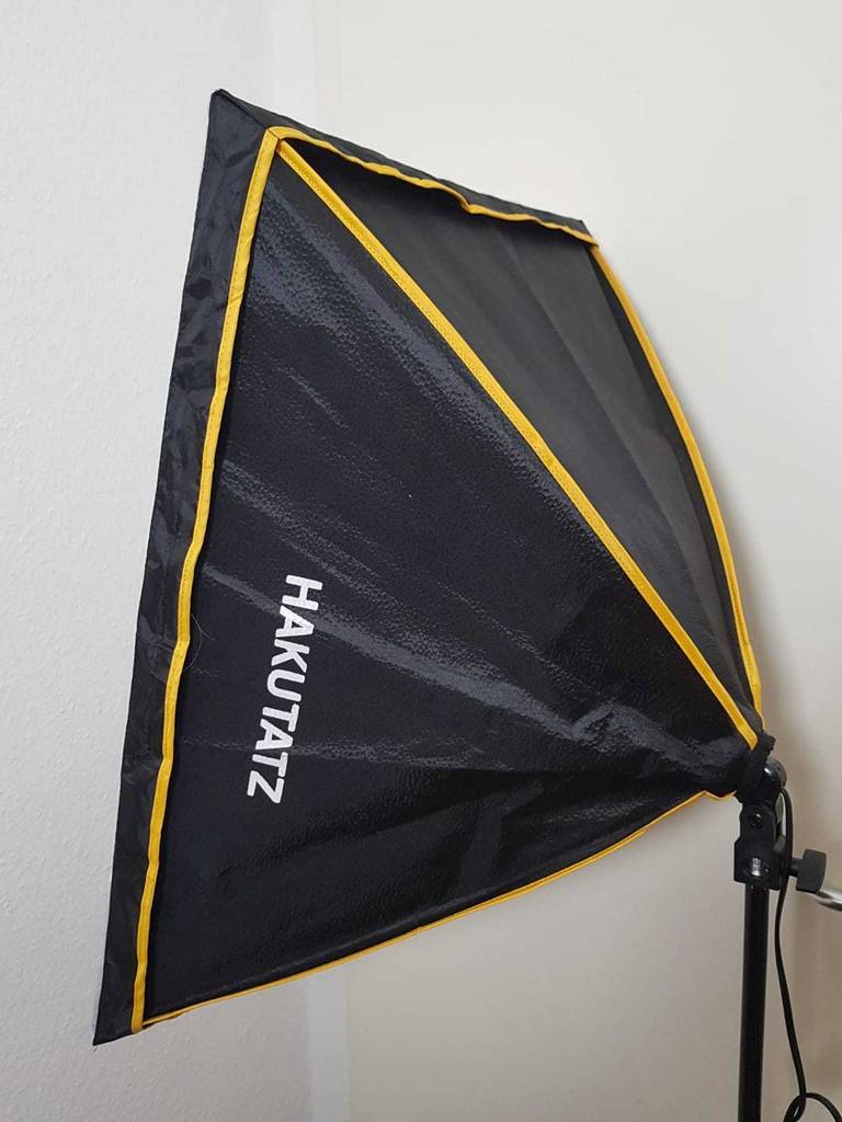 Seitenansicht einer Hakutatz-Softbox im Test, die mit einem schwarzen Schirm und Gestell versehen ist und vor einer weißen Wand steht.