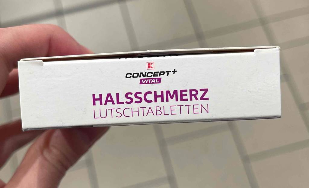 Eine Hand hält die schmale Seite von Kaufland Concept+Vital-Halsschmerztabletten im Test in die Photokamera.