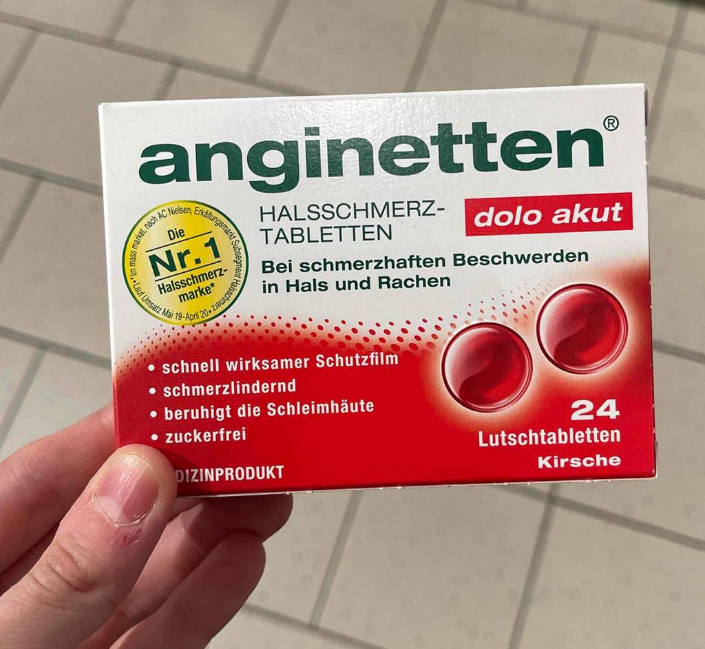 Eine weiß-rote Verpackung, inklusive 24 Stück Halsschmerztabletten im Test, werden von einer Hand gehalten.