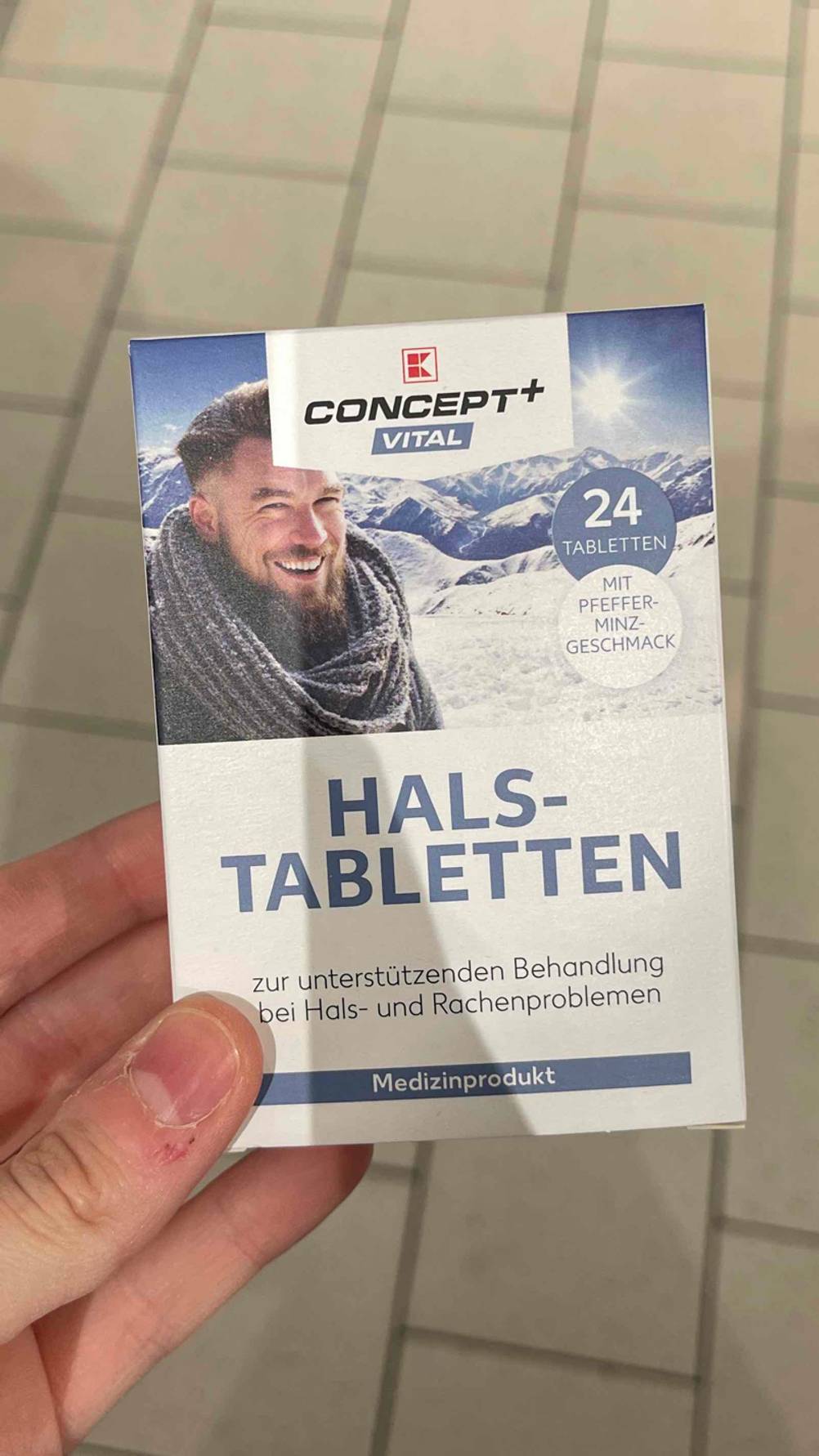 Eine Hand hält eine Packung getestete Halstabletten mit Pfefferminze.
