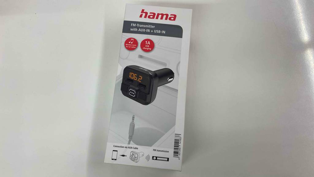 Zum Test bereit ein Hama-FM-Transmitter in seiner Verpackung auf einem hellen Untergrund.