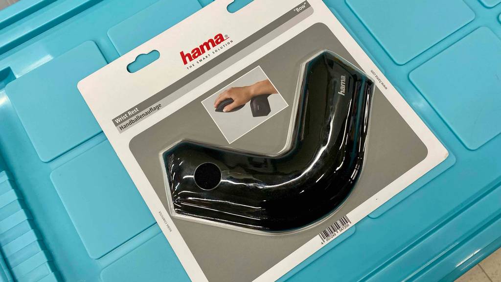 Ein original verpackte, schwarze Handballenauflage von Hama liegt auf einem hellblauen Untergrund.