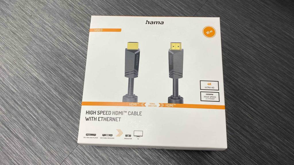 Eine weiße Verpackung mit dem getesteten Hama-HDMI-Kabel in 10 Meter Läange inklusive goldener Stecker liegt auf einem grauen Boden.