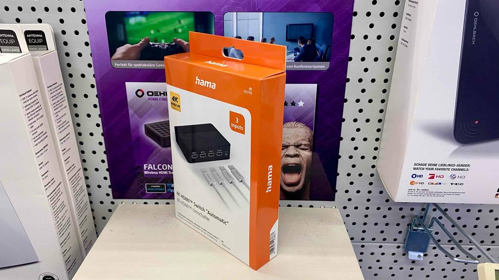 HDMI-Switch im Test: ein Gerät von Hama steht verpackt schräg vor anderen Geräten auf hellem Regal.
