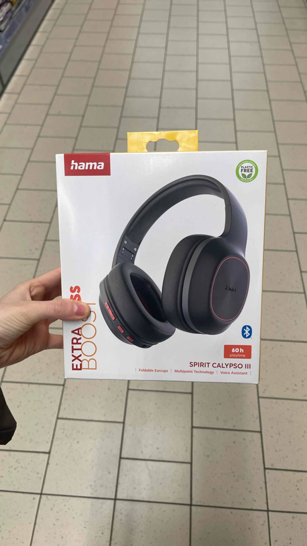 Eine Hand hält die Verpackung mit dem Hama-Kopfhörer im Test über einem weißen Fliesenboden. 
