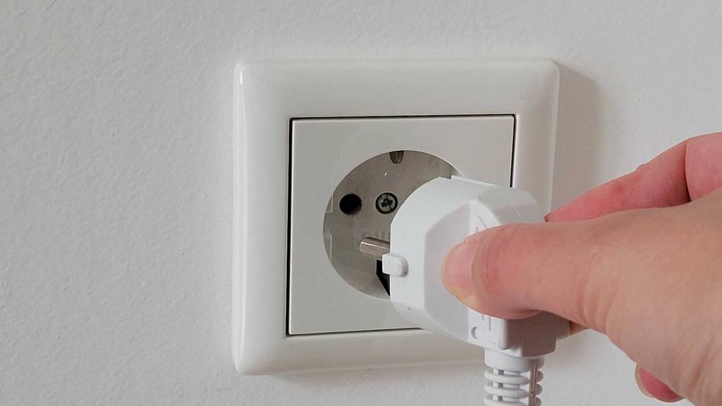 Steckdosenleiste-Test: Hand steckt Stecker einer Steckdosenleiste in eine Steckdose an der Wand.