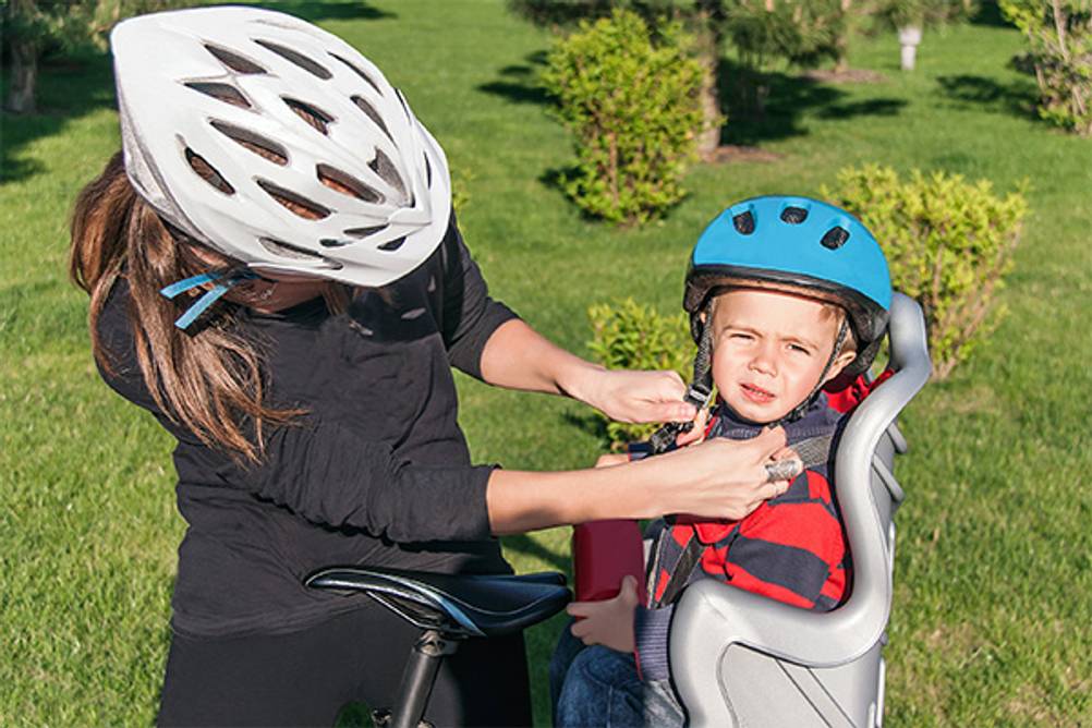 Hamax-Fahrradsitz im Test: Eine Mutter, die ihrem Kind einen Helm anlegt.