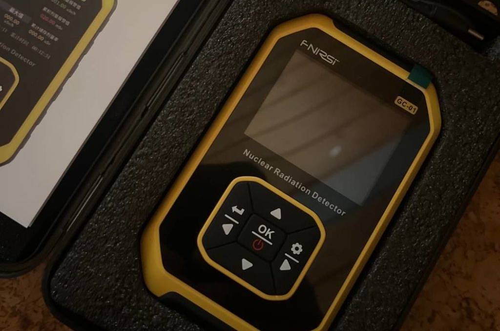 Schwarzer-goldener Geigerzähler im Test liegt in seinem Aufbewahrungs-Koffer auf einer Korkfläche.