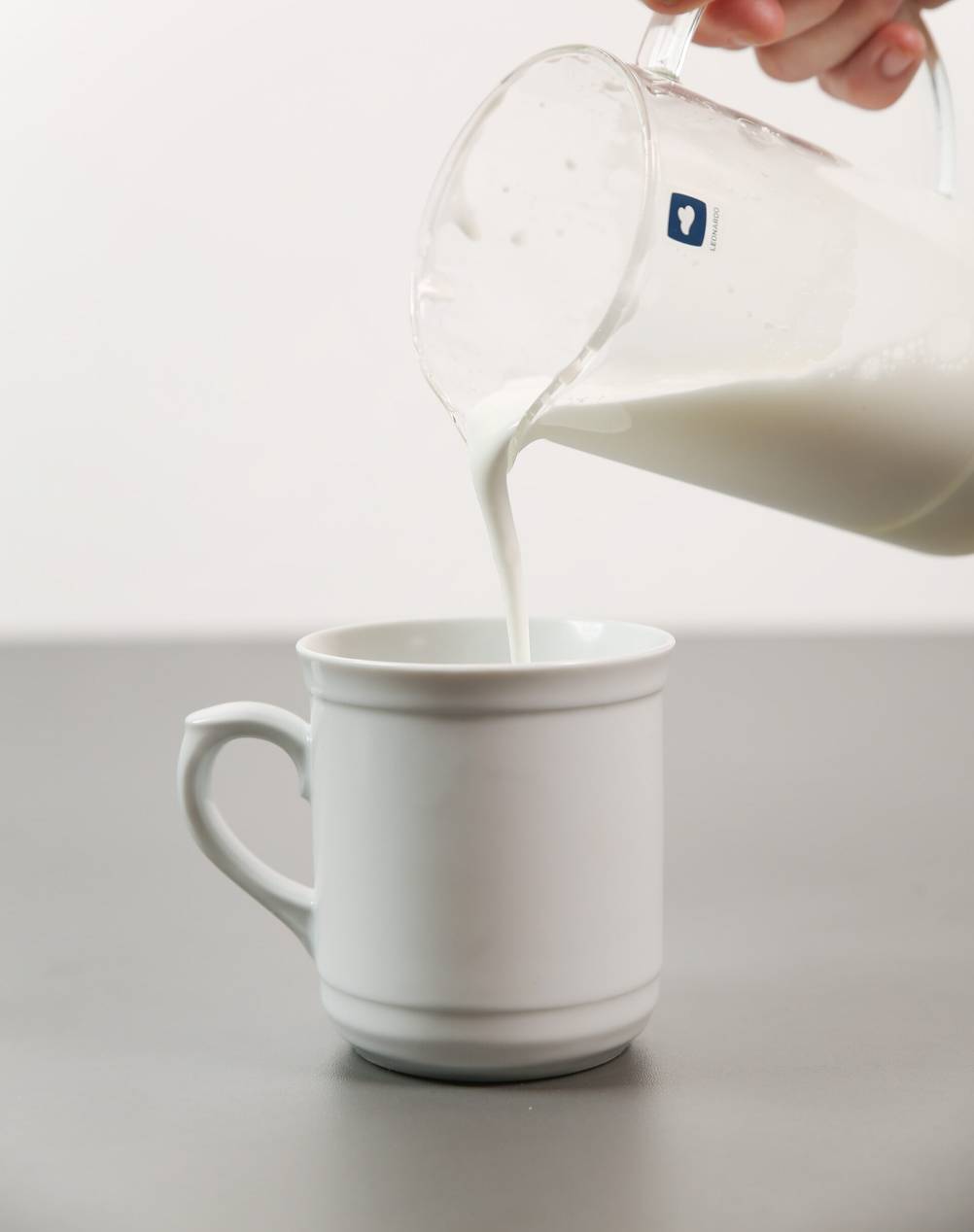 Hand-Milchaufschäumer im Test: Eine Person gießt Milchschaum aus einem Glas-Milchaufschäumer in eine weiße Tasse.