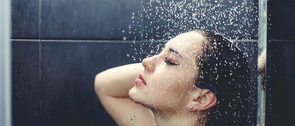 Junge Frau unter der Dusche mit Handbrause