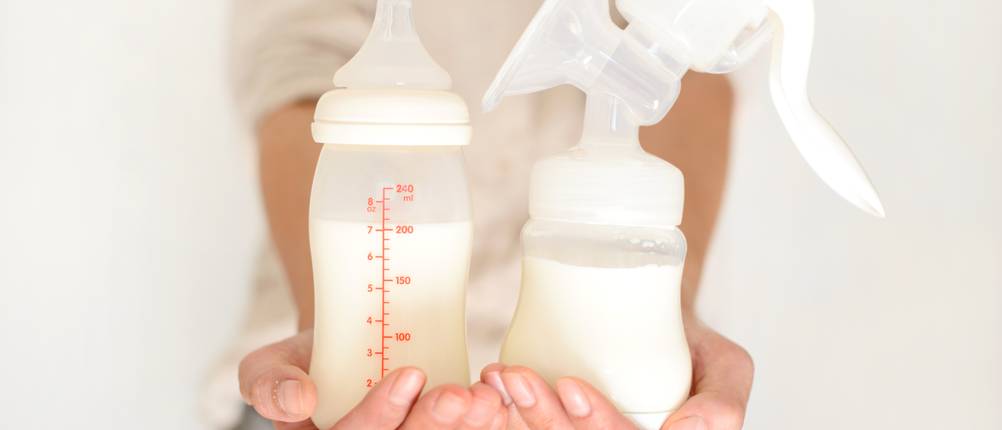 Handmilchpumpe im Test: Frau hält Handmilchpumpe und Fläschchen mit Milch in den Händen