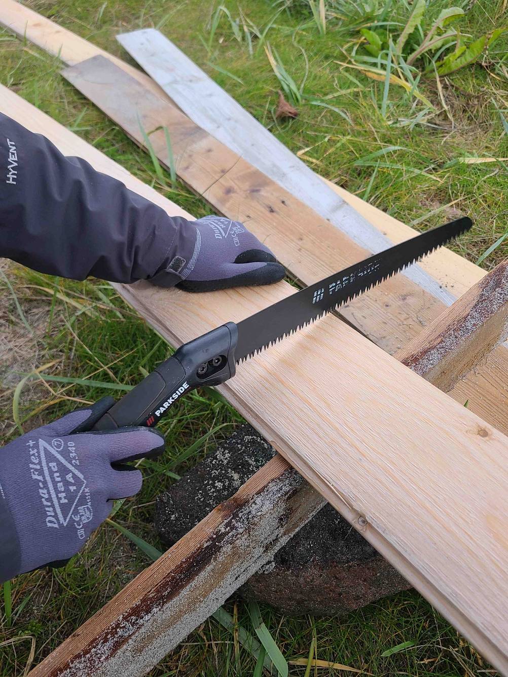 Eine Hand sägt mit der getesteten Handsäge ein Brett.