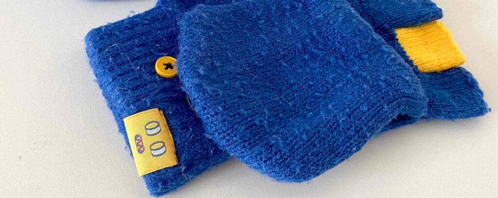 Herren-Handschuhe im Test: Nahaufnahme des gelben Markenzeichens von gestrickten blauen Handschuhen.