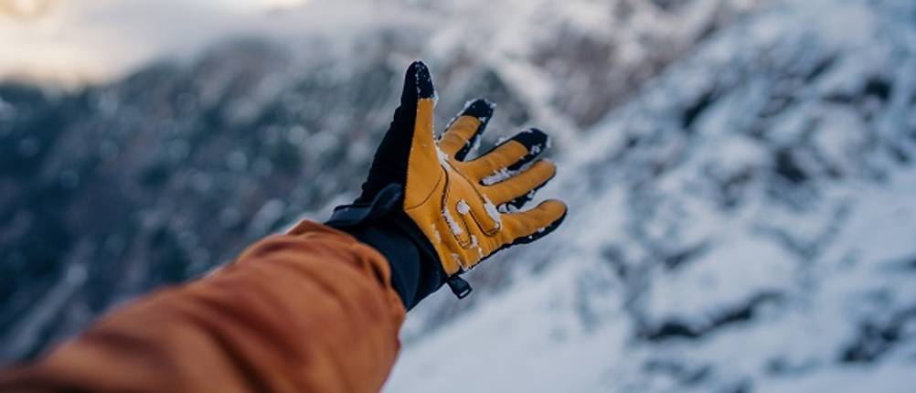 Herren-Handschuhe im Test: Mensch, der mit Handschuhen auf schneebedeckte Berge zeigt
