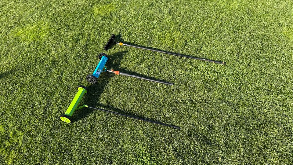 Drei Handvertikutierer liegen nebeneinander im Gras.