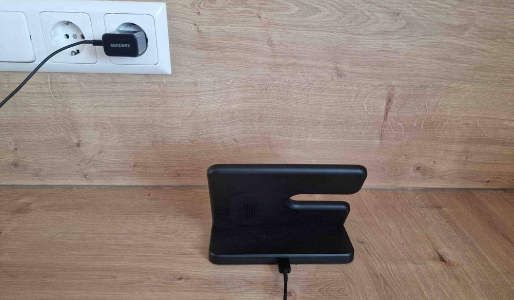 Eine schwarze Samsung-Handy-Ladestation im Test steht auf einem Holztisch und ist an eine Steckdose angeschlossen.