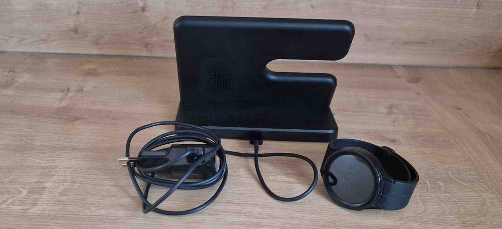 Schwarze getestete Handy-Ladestation steht inklusive Kabel hinter einer schwarzen Smartwatch auf einem Holztisch.