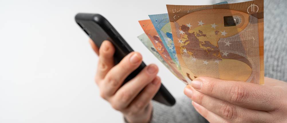 Handy-verkaufen-Test: Eine Frau hält ein Smartphone und mehrere Geldscheine in der Hand.