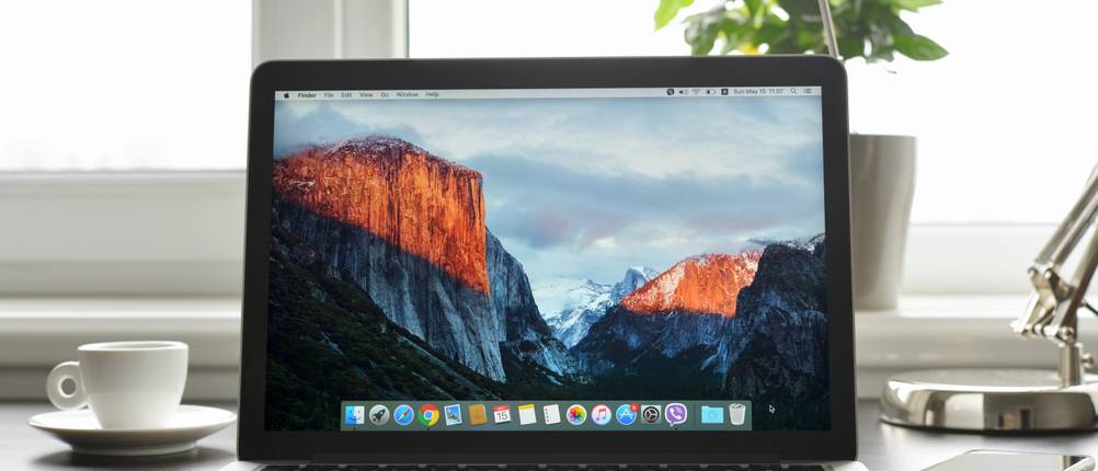 Ein Apple MacBook steht auf einem Tisch, im Hintergrund ist ein Fenster zu sehen.