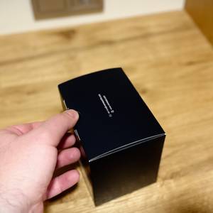 Die Auto-Handyhalterung von Vanmass ist in einem geschlossenen Karton und eine Hand öffnet diesen.