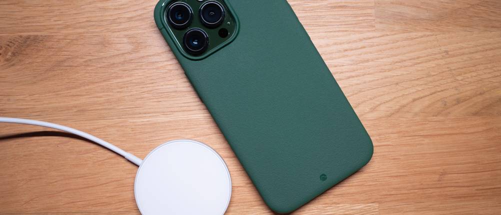 Ein iPhone mit einem grünen Case und ein MagSafe-Ladegerät liegen auf einem Holztisch.