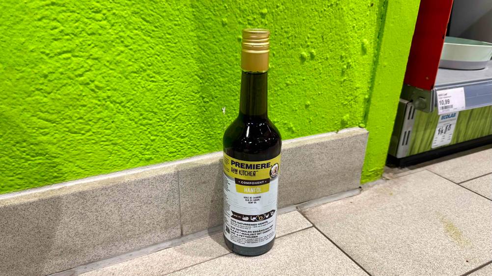 Vor einer grünen Wand auf dem Boden steht eine Flasche des Hanföl Hund im Test.