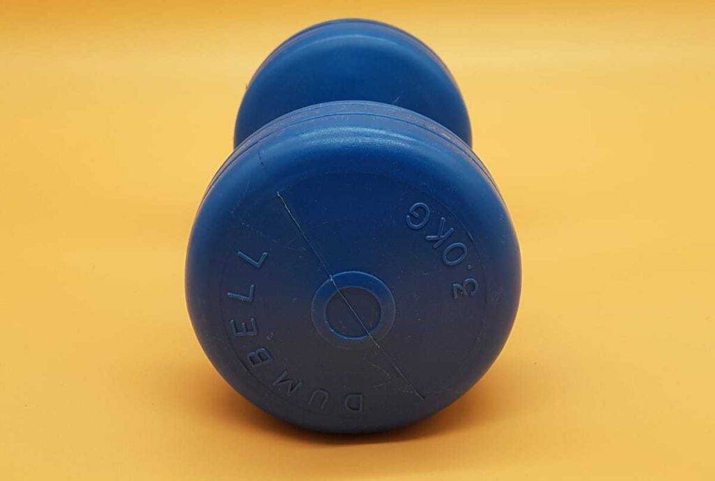 Seitenansicht auf ein blaues Drei-Kilogramm-Gewicht der Marke Dumbell, das auf einer pfirsichfarbenen Oberfläche liegt.