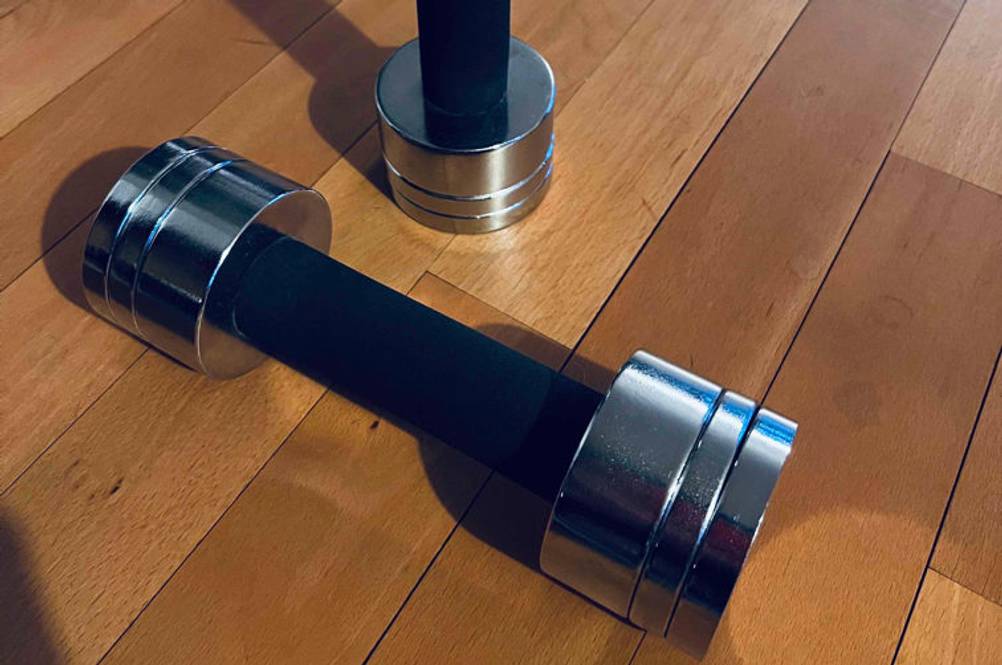 1 kg Hanteln im Test: eine Hantel aus Metall liegt quer vor einer aufrecht stehenden.