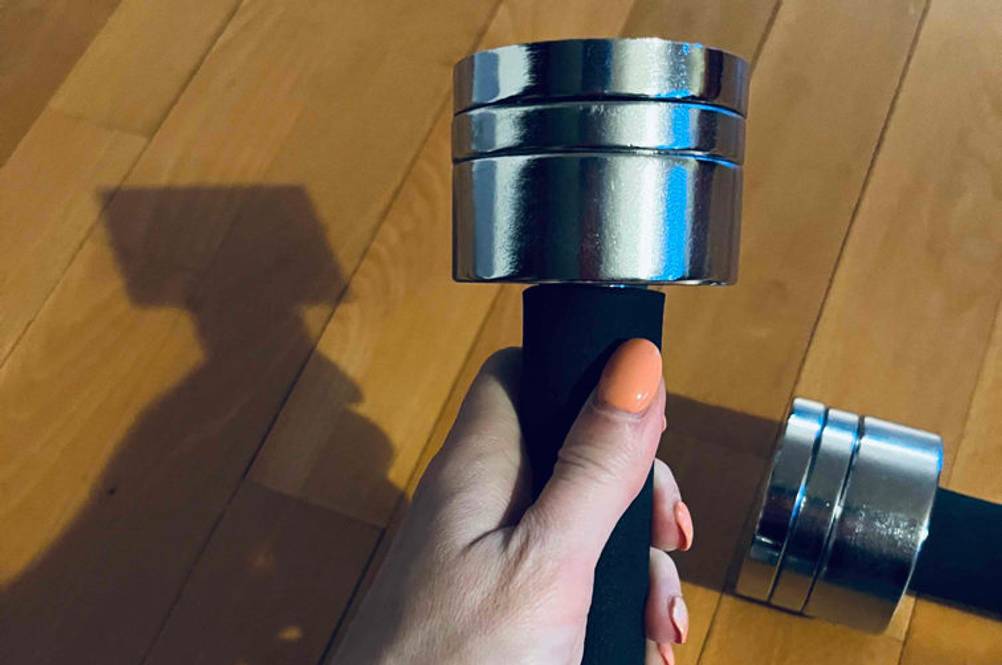 Hanteln 1 kg im Test: Hand hält eine Metall-Hantel über einem Boden, auf dem eine zweite halb ins Bild ragt.