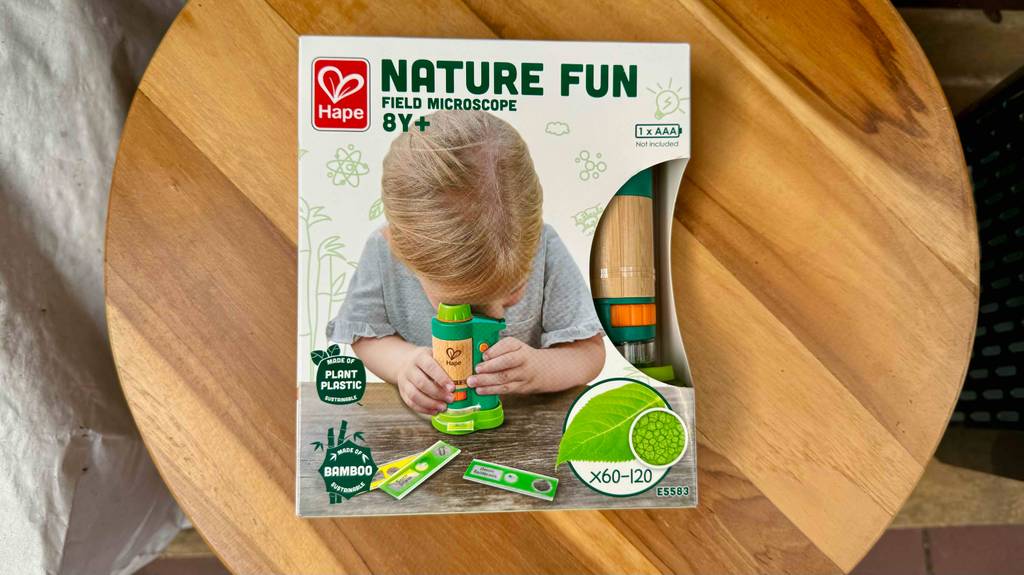 Ein Kinder-Mikroskop liegt in Originalverpackung zum testen auf einem runden Holztisch.