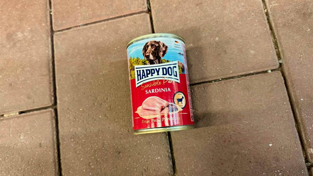 Eine Dose getestetes Happy Dog-Nassfutter liegt auf einem Steinboden.