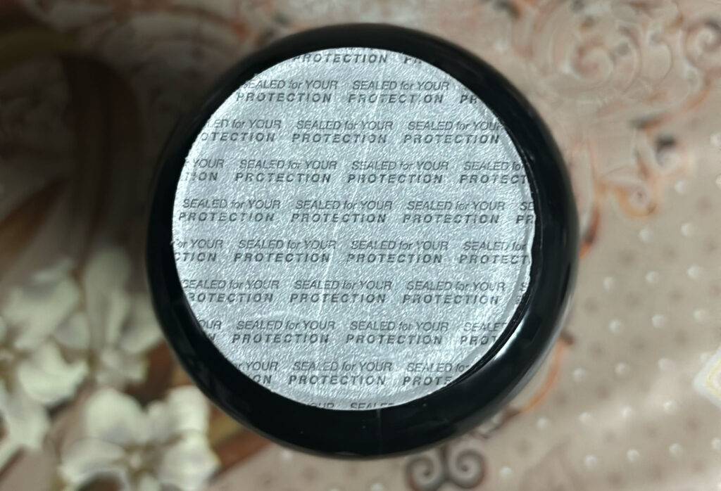 Glucosamin-Test: Nahaufnahme von oben auf den Vakuumschutz eines runden Flakons auf einer beige gemusterten Tischdecke.