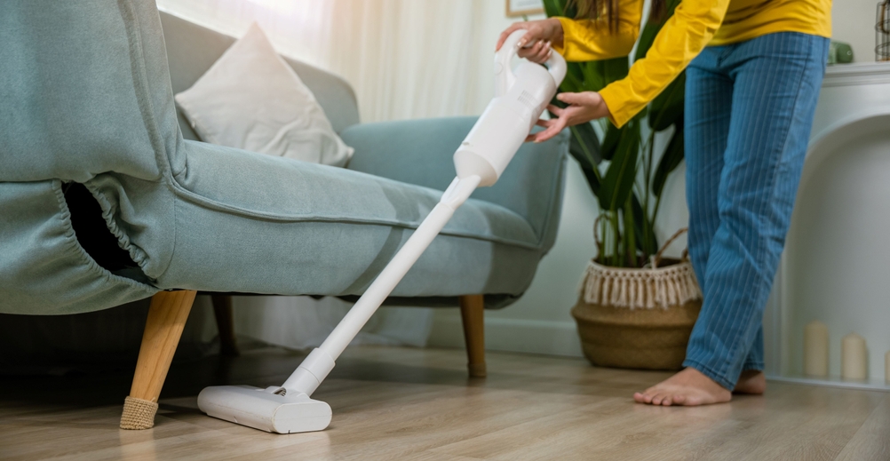 Eine Frau saugt unter einem Wohnzimmersofa.