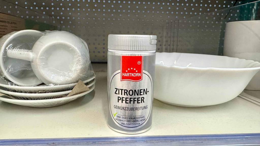 Ein Gewürzstreuer von Hartkorn mit getestetem Zitronensalz steht auf einem Regal mit weißem Geschirr.