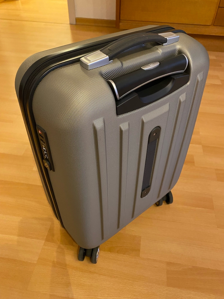 Rückseite eines getesteten Hartschalenkoffers mit Griffen auf einem Holzboden.