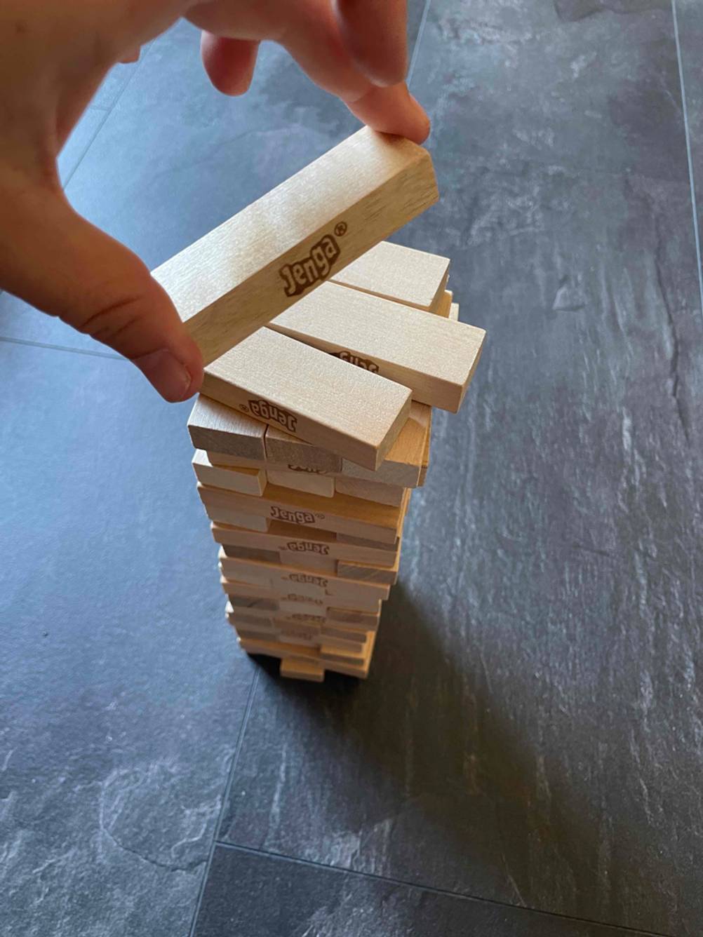 Eine Hand hält einen Holzstein über einen gebauten Turm eines Geschicklichkeitsspiels im Test.