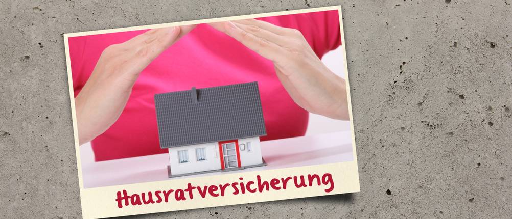 Hausratversicherungen im Test: Auf einem grauen Tisch ist ein Bild eines Hauses mit der Aufschrift Hausratversicherung.