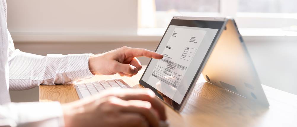 Hausratversicherungen im Test: Eine Person sitzt an einem Tablet und zeigt auf eine Rechnung.