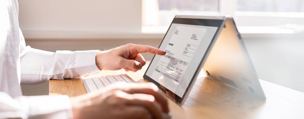 Eine Person sitzt an einem Tablet und zeigt auf eine Rechnung.