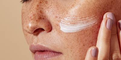 Eine Nahaufnahme des Gesichts einer Frau mit Sommersprossen, die eine Creme aufträgt.