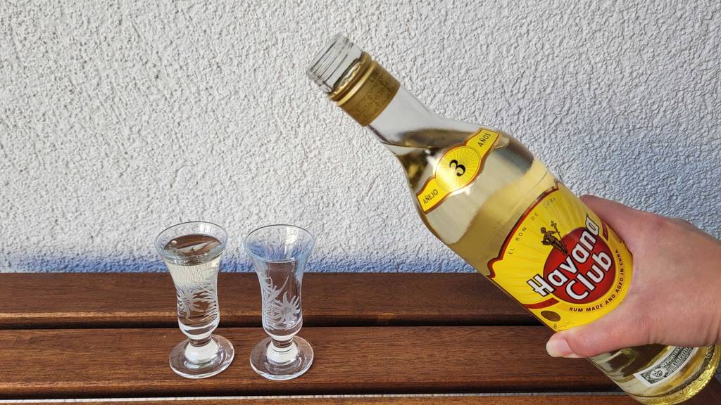 Weißer Rum-Test: Eine Hand schenkt aus einer Flasche in zwei Gläser ein.