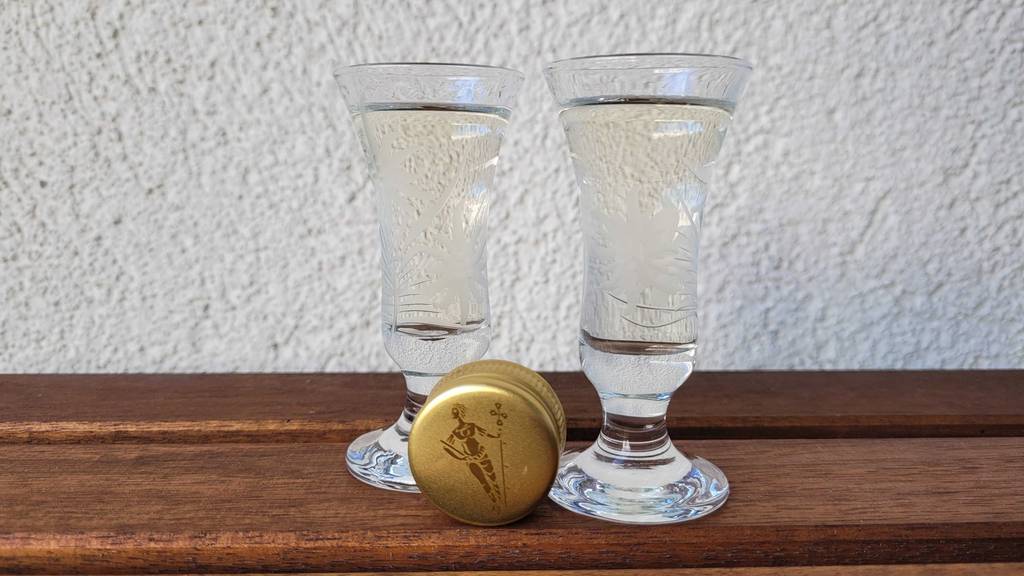 Weißer Rum im Test: Zwischen zwei gefüllten Gläsern liegt der Deckel einer Flasche.