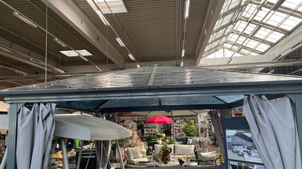 Pavillon-Metall-Test: Ansicht des Dachbereichs eines im Gartencenter aufgebauten, grauen Pavillons inklusive anthrazitfarbener Vorhänge.