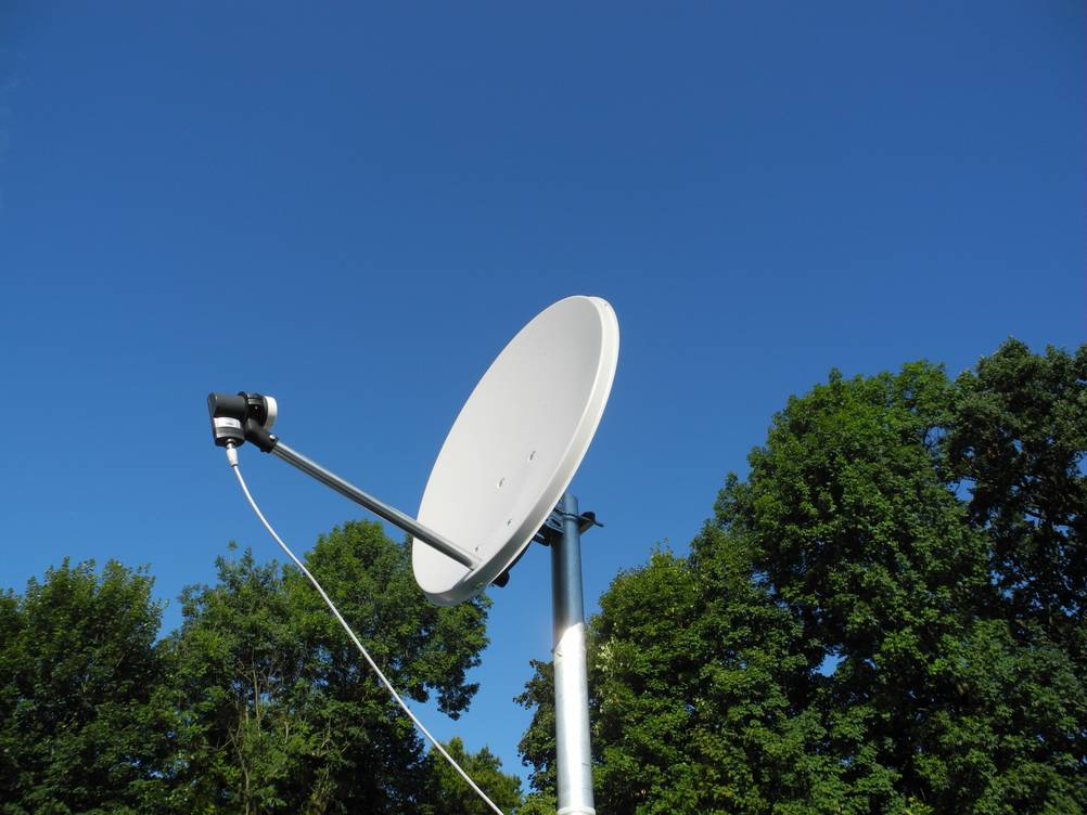 HD-Receiver im Test: Eine Satellittenschüssel vor Bäumen und blauem Himmel.