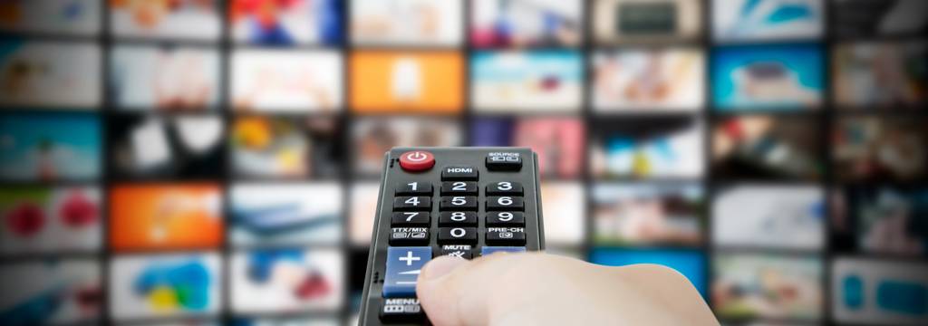 4K-HDMI-Extender im Test: Eine Fernbedienung und im Hintergrund ein Display mit zahlreichen Video-Bannern.