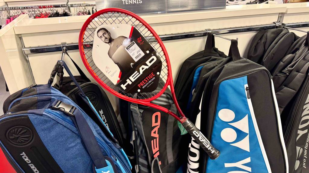 Ein getesteter Head-Tennisschläger liegt quer über einem Hängeregal mit Taschen.