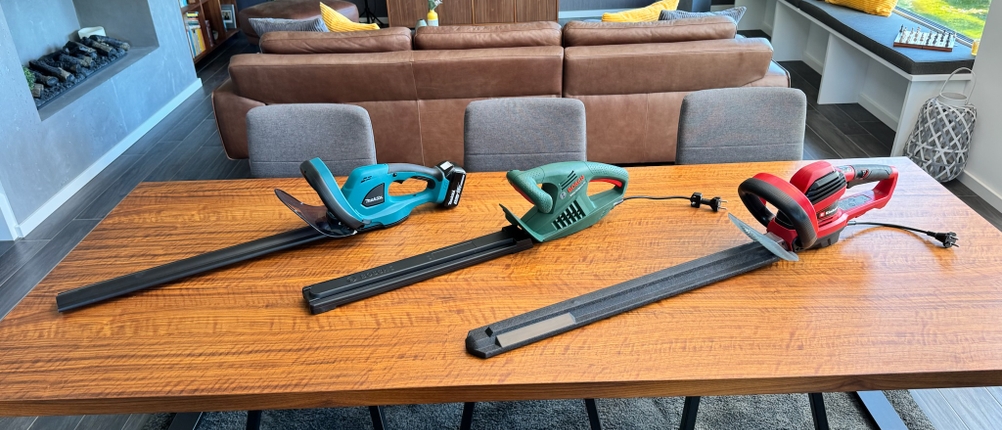 Drei Heckenscheren liegen auf einem Holztisch.